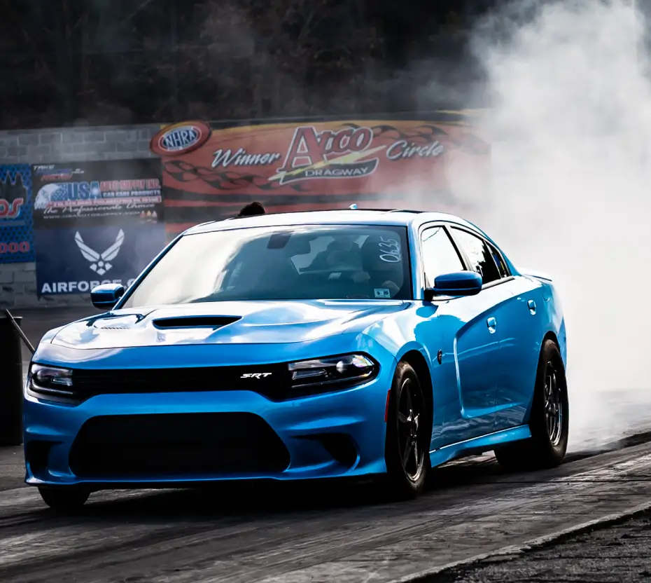 Blue Dodge SRT drag racing with banners in the background.